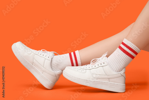 Foto Legs of young woman in stylish white sneakers on orange background