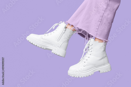 Legs of young woman in stylish white leather boots on lilac background photo