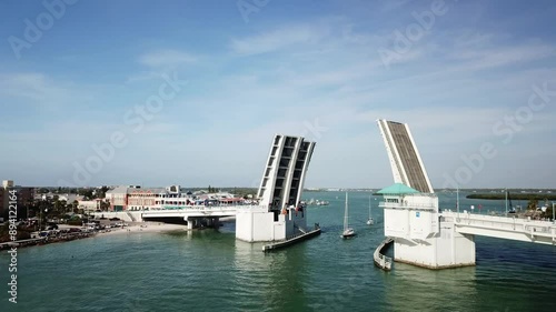 Johns Pass drawbridge in Florida raised to allow boats to pass, with buildings and clear sky in the background.