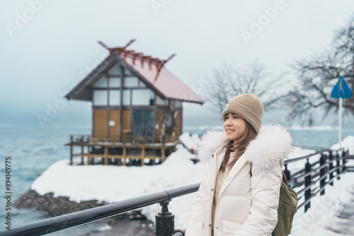 Woman tourist sightseeing Kansa Shrine and Lake Tazawa in winter. Traveler travel in Semboku city, Akita Prefecture, Japan. Landmark for tourist attraction in Tohoku region. Japan travel and vacation photo