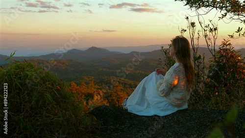Wallpaper Mural Young woman in white dress sitting on mountaintop at sunset, enjoying scenic view of rolling hills and distant mountains. Tranquility and Nature. Torontodigital.ca