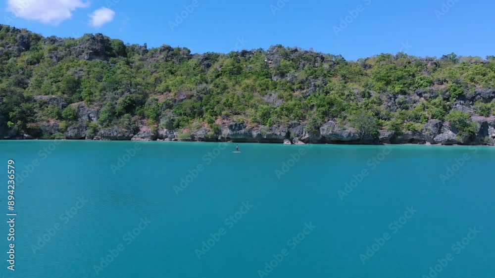 Man rowing on a standup paddle board in a calm sea with a beautiful view of the island Man rowing on a standup paddle board in a calm sea with a beautiful view of the island