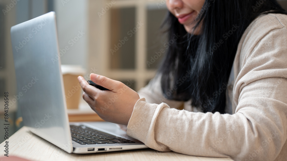 A close-up image of an Asian woman using her smartphone while working remotely in a coffee shop. A close-up image of an Asian woman using her smartphone while working remotely in a coffee shop.