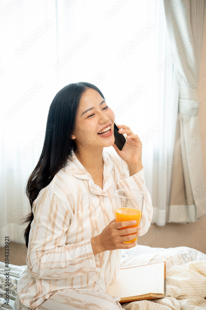 A beautiful, carefree Asian woman in pajamas is enjoying talking on the phone in bed in her bedroom. A beautiful, carefree Asian woman in pajamas is enjoying talking on the phone in bed in her bedroom.