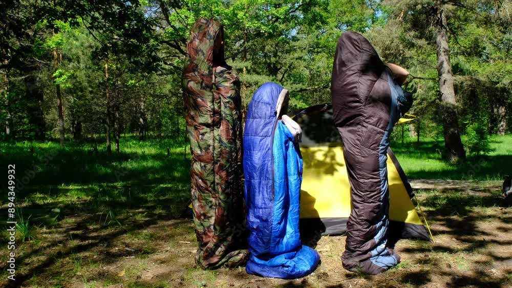 Family of tourists from a father, mother and daughter pose and Funny dancing in sleeping bags near a tent. Family outdoor recreation, camping, hiking equipment. Family of tourists from a father, mother and daughter pose and Funny dancing in sleeping bags near a tent. Family outdoor recreation, camping, hiking equipment.