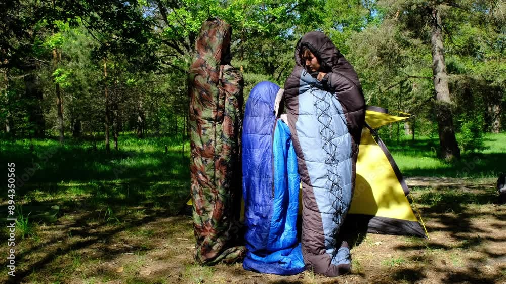 Family of tourists from a father, mother and daughter pose and Funny dancing in sleeping bags near a tent. Family outdoor recreation, camping, hiking equipment. Family of tourists from a father, mother and daughter pose and Funny dancing in sleeping bags near a tent. Family outdoor recreation, camping, hiking equipment.
