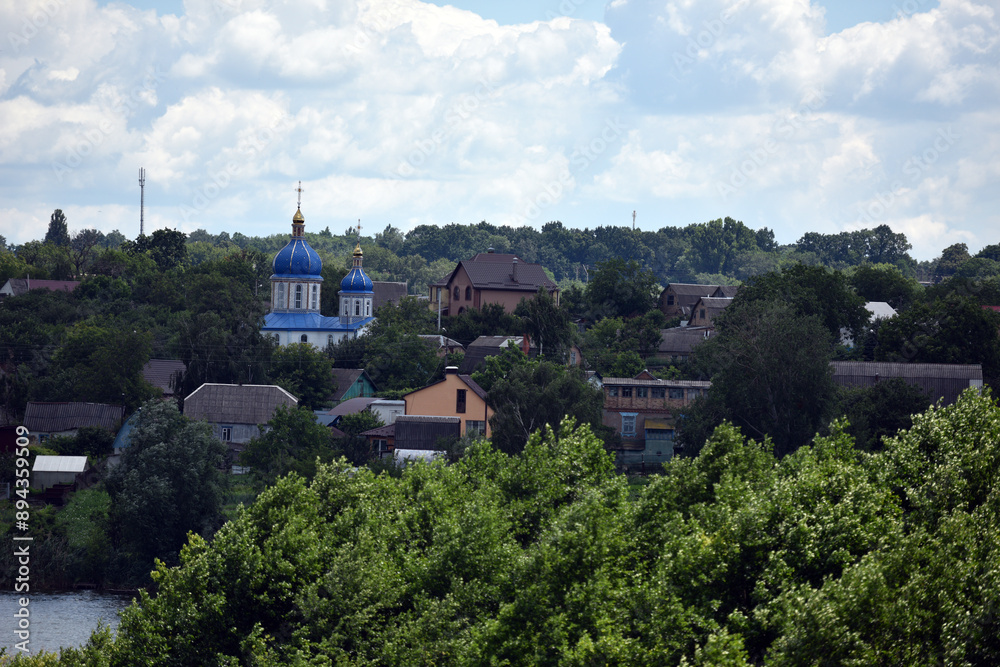 Fototapeta premium church. view of the Ukrainian church in the village. religion, Christianity. church holidays. crosses on the domes. no people. roofs of houses. summer or spring time. Orthodox temple.