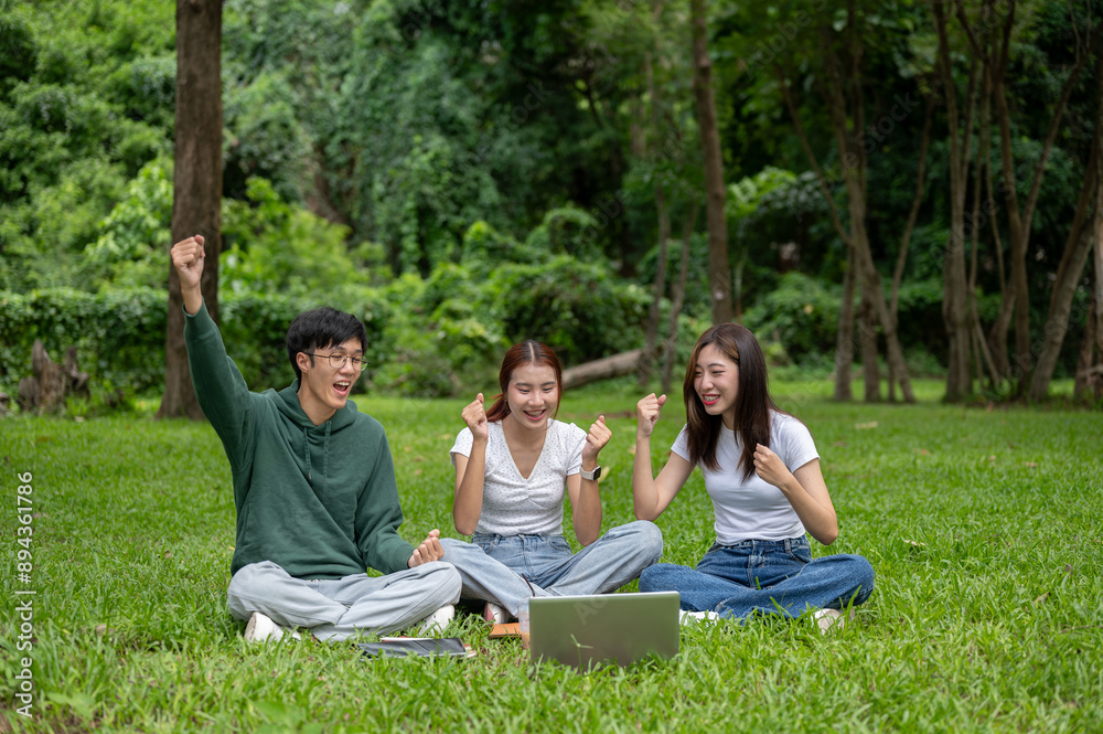 Cheerful students is checking their exam scores on a laptop and celebrating together in a park.