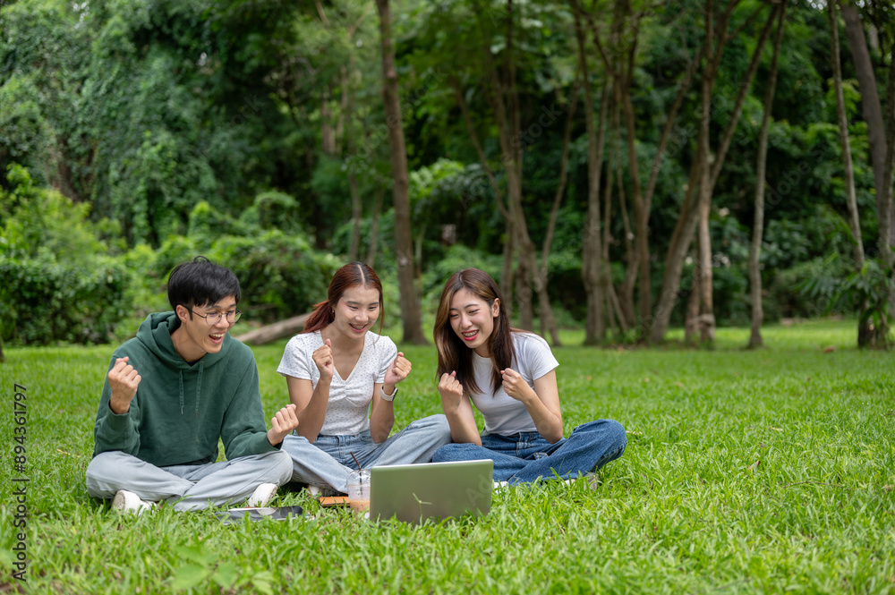 Cheerful students is checking their exam scores on a laptop and celebrating together in a park. Cheerful students is checking their exam scores on a laptop and celebrating together in a park.