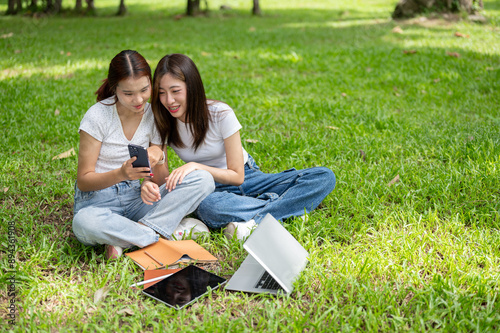 Two lovely Asian female friends are enjoying talking and watching something on a smartphone. © bongkarn