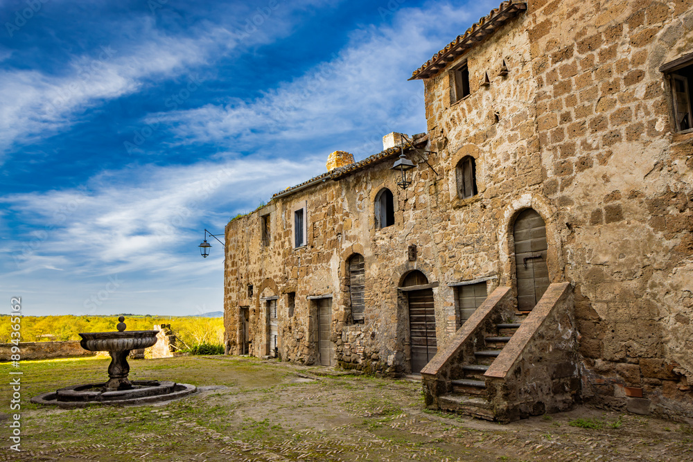 Naklejka premium A glimpse of the ancient medieval village of Montecalvello, Viterbo, Italy. The internal courtyard of the castle with the ancient stone and brick buildings and the fountain in the center.