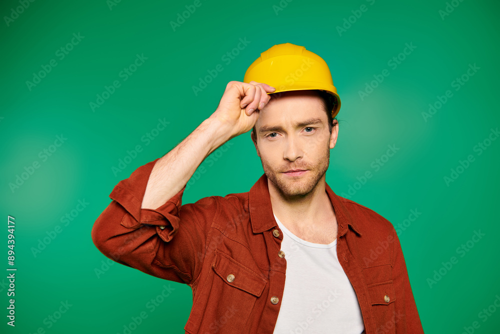 A handsome male worker in uniform and tools sporting a yellow hard hat on a green backdrop. A handsome male worker in uniform and tools sporting a yellow hard hat on a green backdrop.