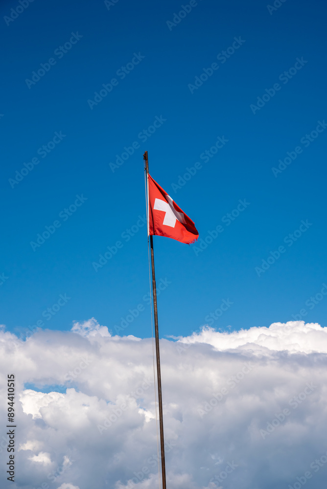 swiss flag on a long pole with the blue sky and cumulus clouds