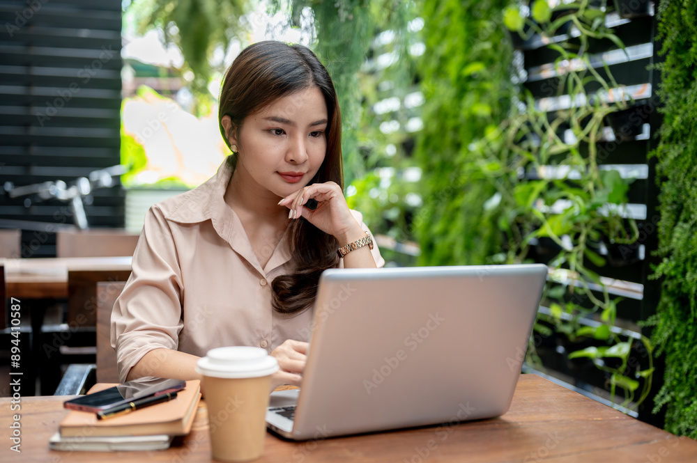 A confident Asian businesswoman working remotely at a cafe, focusing on working on her laptop. A confident Asian businesswoman working remotely at a cafe, focusing on working on her laptop.