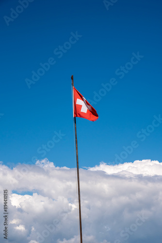 swiss flag on a long pole with the blue sky and cumulus clouds