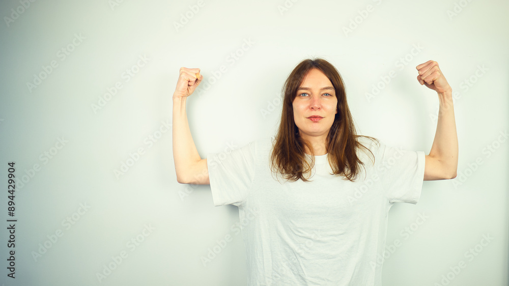 Portrait of beautiful Caucasian young female model with blue eyes and white shirt flexing her biceps, isolated on white background, copy space area Portrait of beautiful Caucasian young female model with blue eyes and white shirt flexing her biceps, isolated on white background, copy space area