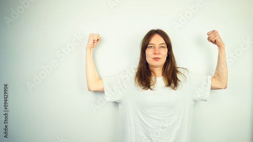 Obraz na płótnie Portrait of beautiful Caucasian young female model with blue eyes and white shirt flexing her biceps, isolated on white background, copy space area w salonie