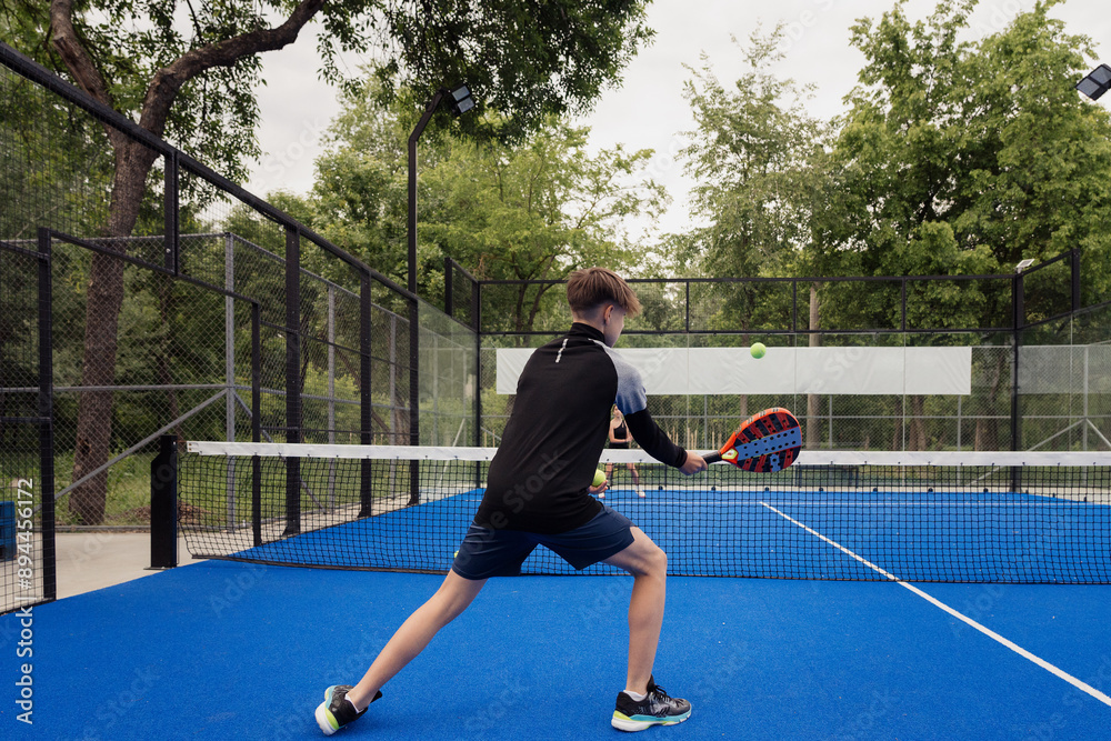 Obraz premium Young man in action playing padel tennis on an outdoor court. The player is focused and engaged, showcasing athletic performance.
