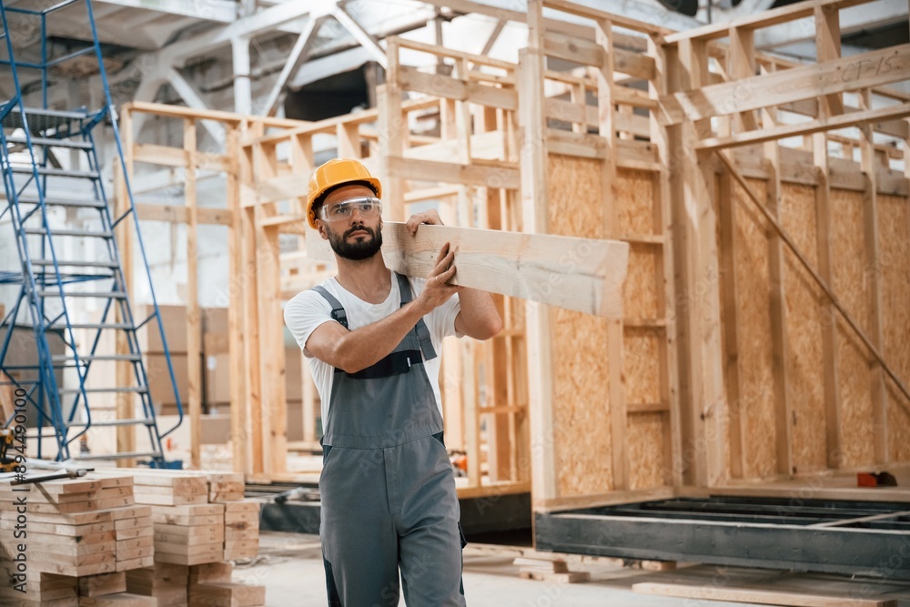 Walking, holding plank. Industrial worker in wooden warehouse Walking, holding plank. Industrial worker in wooden warehouse
