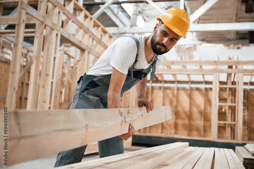 Front view, holding plank. Industrial worker in wooden warehouse