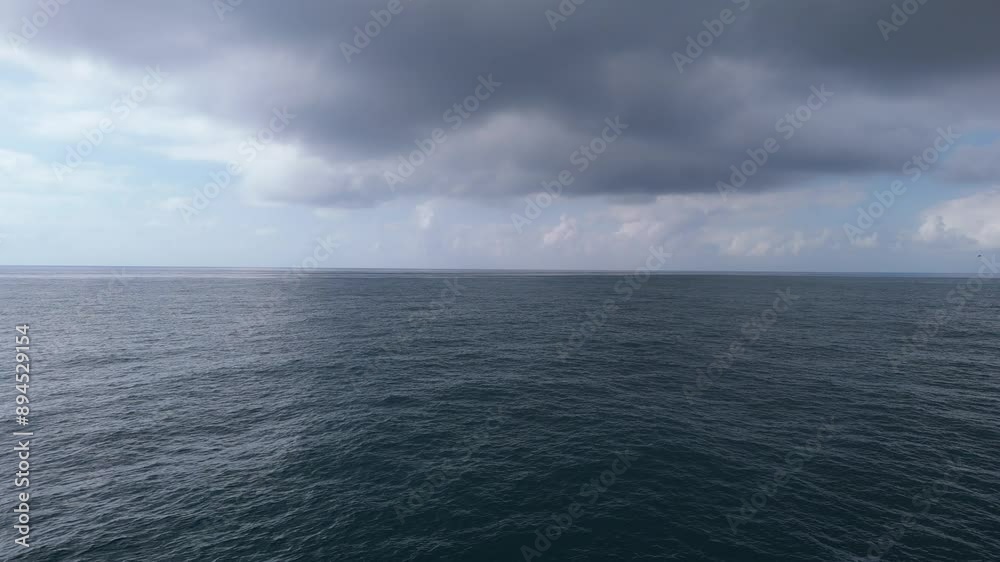 Slow-motion drone flight over the open ocean. Waves ripple under a cloudy sky with sunlight peeking through. The horizon blends sky and water. Slow-motion drone flight over the open ocean. Waves ripple under a cloudy sky with sunlight peeking through. The horizon blends sky and water.