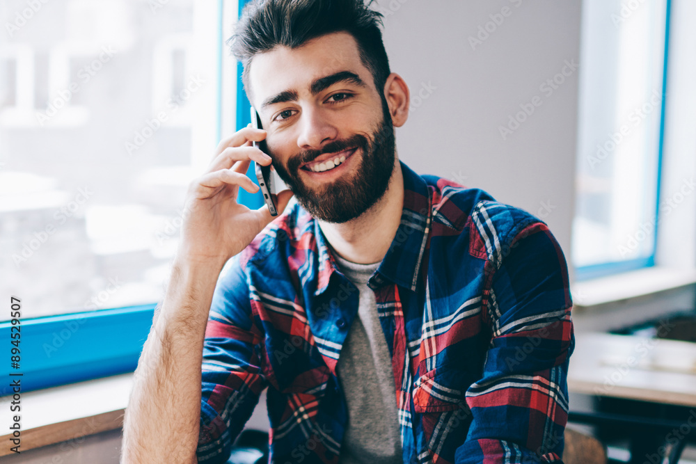 Portrait of successful smiling hipster guy calling to friend via mobile application while sitting at university campus and looking at camera, smiling man casual dressed communicated via smartphone Portrait of successful smiling hipster guy calling to friend via mobile application while sitting at university campus and looking at camera, smiling man casual dressed communicated via smartphone