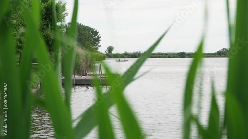 Boats tied to shore of a lake seen from behind tall green grass