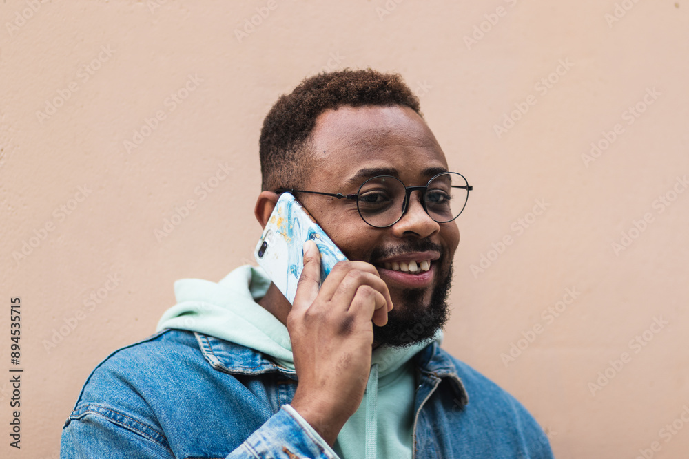Satisfied black man with thick bristle looks aside, has phone conversation, keeps mobile phone near ear, dressed inn fashionable outfit, looks aside, isolated over brown wall with empty space Satisfied black man with thick bristle looks aside, has phone conversation, keeps mobile phone near ear, dressed inn fashionable outfit, looks aside, isolated over brown wall with empty space