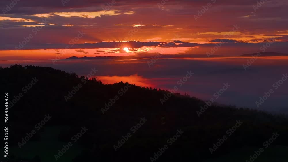 LENS FLARE, SILHOUETTE: A serene sunset over misty hills and valleys, with vibrant colours lighting up the sky. Ethereal view of hilly landscape under colourful clouds as the day transitions to night. LENS FLARE, SILHOUETTE: A serene sunset over misty hills and valleys, with vibrant colours lighting up the sky. Ethereal view of hilly landscape under colourful clouds as the day transitions to night.
