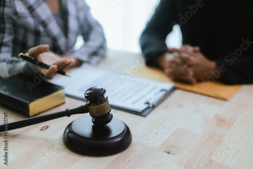 In a lawyer's office, a businessman consults an attorney for legal advice on a contract. The gavel symbolizes authority and justice. The lawyer explains the legislation and provides guidance on the ag © Witoon
