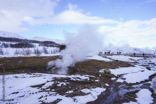 Winter view of tourists standing on snow covered hot spring with vapor near Geysir, Iceland 