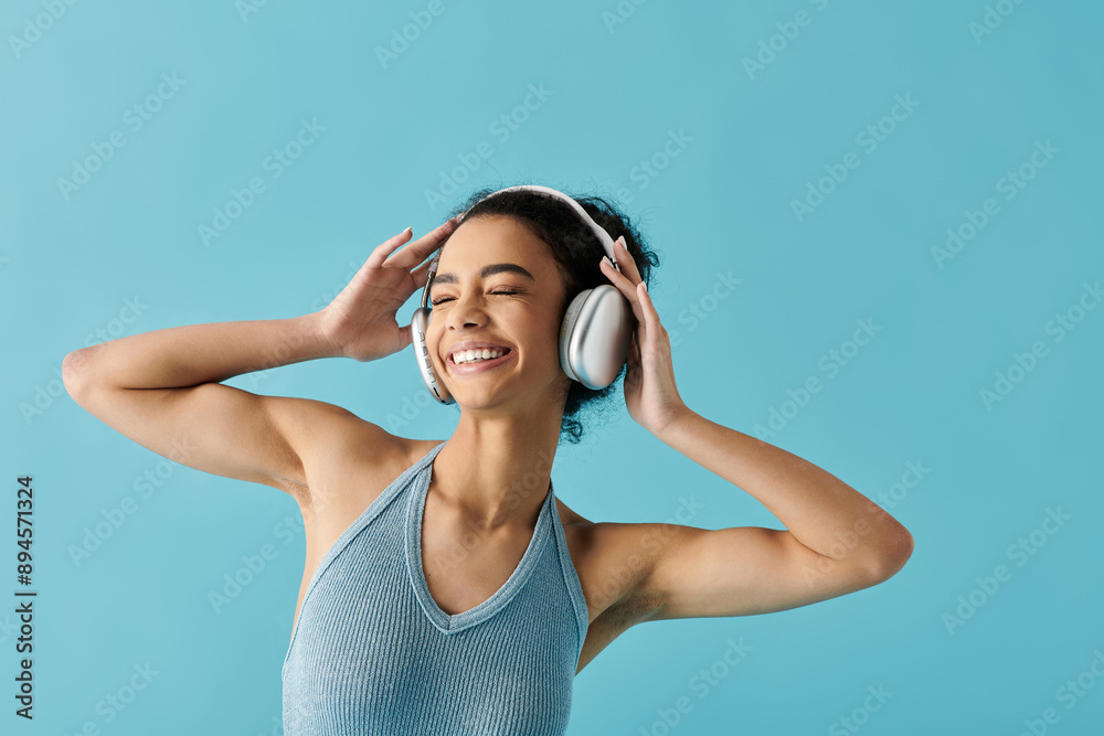 A young woman in a blue dress stands against a bright blue backdrop, her eyes closed in bliss as she listens to music through headphones.