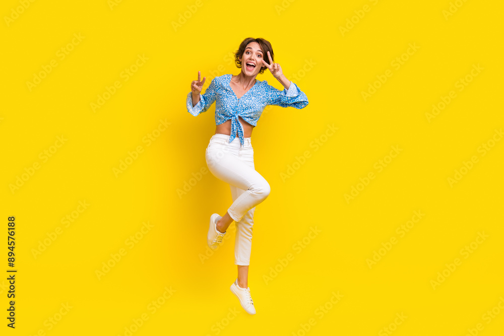 Full length photo of eccentric ecstatic lovely girl dressed blue top showing v-sign on eye jumping isolated on yellow color background Full length photo of eccentric ecstatic lovely girl dressed blue top showing v-sign on eye jumping isolated on yellow color background