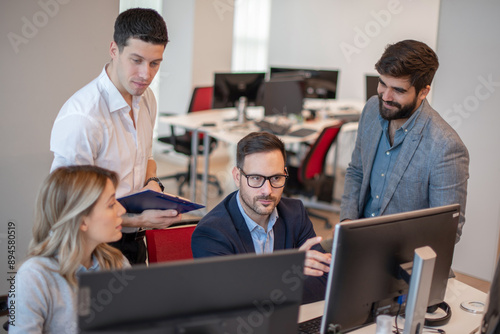 Group of employees working at computer together, discussing Worldwide project at office.