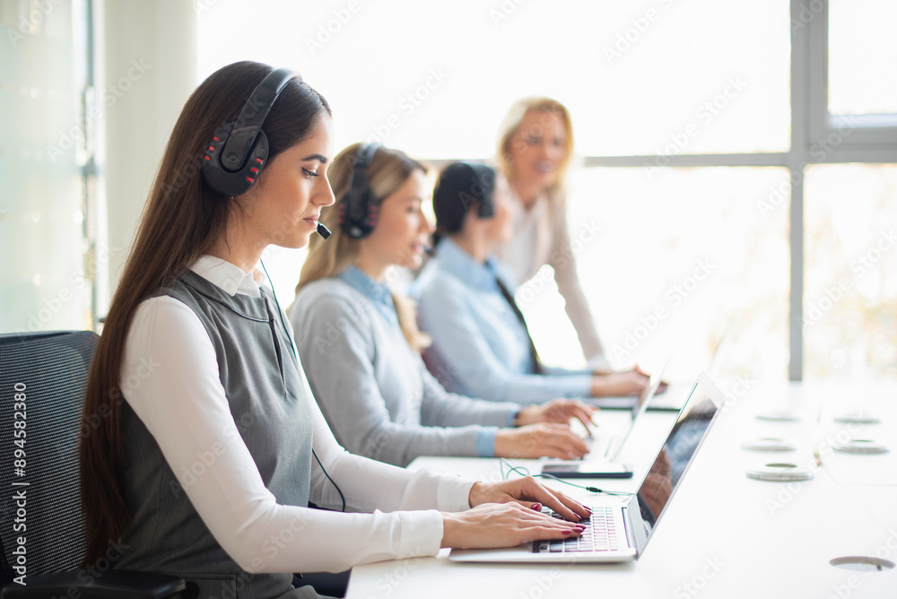 Female helpline call center agent operator in headset working with colleagues in customer care support service office. Female helpline call center agent operator in headset working with colleagues in customer care support service office.