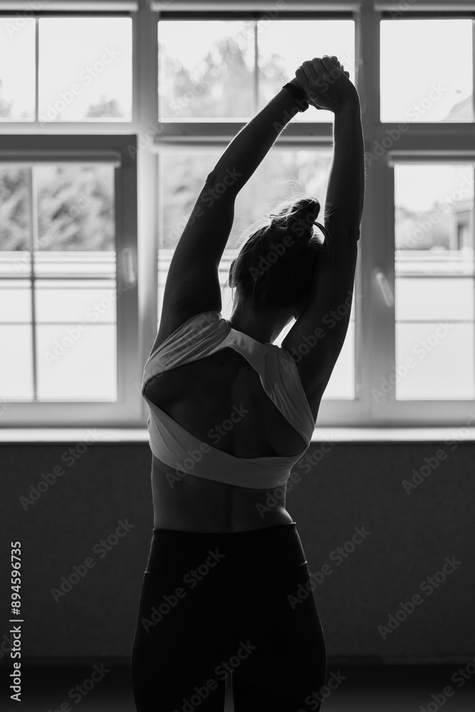 Fototapeta premium Joga, młoda dziewczyna wykonuje ćwiczenia rozciągające przed oknem. Kobieta praktykująca jogę. Rozciąganie, sport. Yoga, young woman practicing yoga, black&white, black and white photography. 