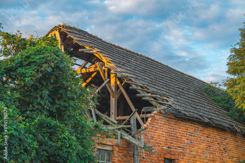 Damaged old brick animal barn. broken, collapsed, damaged roof in the building due to strong wind. a crumbling farm building in the countryside against the background of a beautiful morning sky in sum photo