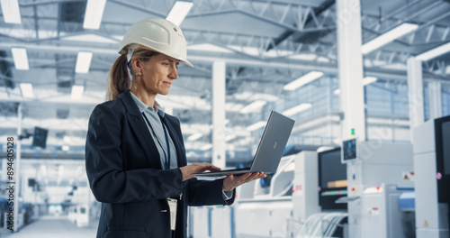 Wallpaper Mural Portrait of a Happy Caucasian Female Engineer in Hard Hat Standing and Using Laptop Computer at Electronic Manufacturing Factory. Technician Thinking About Tasks and Working on Industrial Machinery. Torontodigital.ca