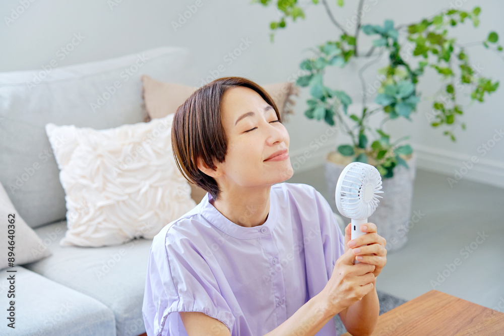 リビングで携帯扇風機を使う女性 リビングで携帯扇風機を使う女性