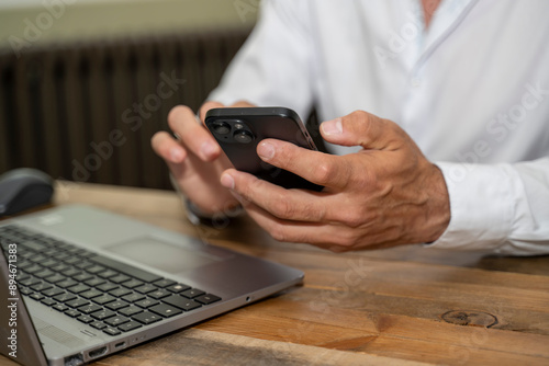 mains d'un homme tenant un téléphone à son bureau devant un ordinateur
