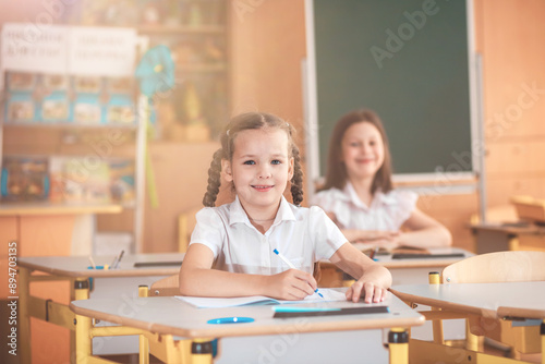 A cute girl sits in a classroom at a table with notebooks and textbooks. The student writes in a notebook. Back to school. School supplies. Student at a lesson, class during a lesson. 