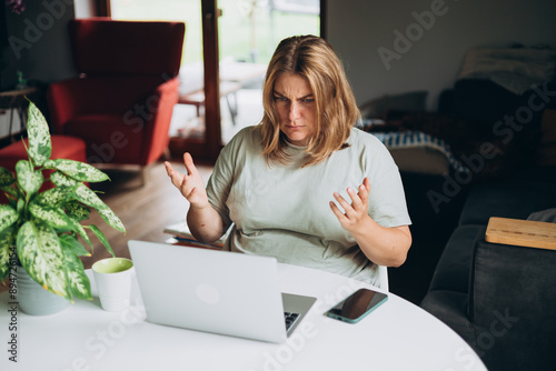Frustrated young adult woman looking in laptop computer in home, fling arms up. Negative people emotion