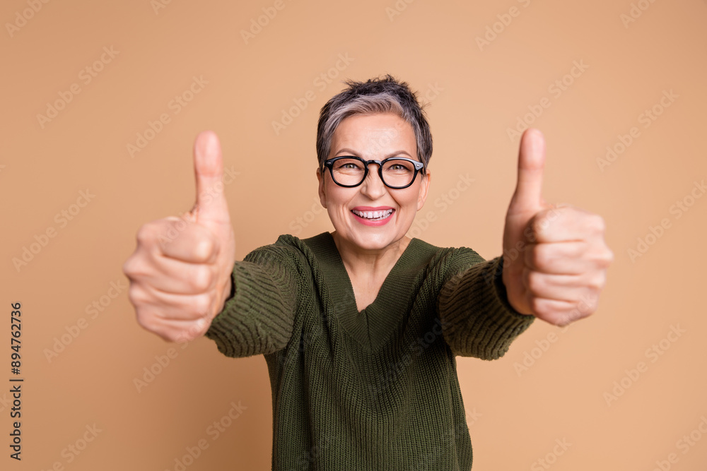 Photo of positive woman with short hair dressed khaki sweater in glasses showing you thumbs up nice job isolated on beige color background Photo of positive woman with short hair dressed khaki sweater in glasses showing you thumbs up nice job isolated on beige color background