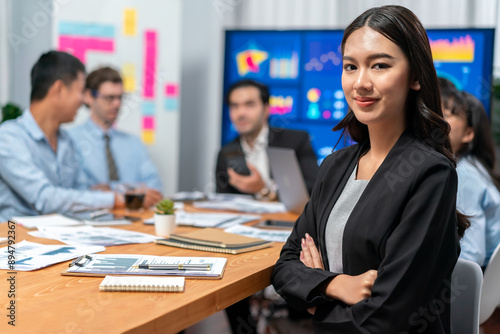 Portrait of happy young asian businesswoman or analyst looking at camera with her colleague analyzing data analysis in dynamic business strategy investment planning meeting. Habiliment