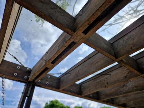 brown glued wooden structure of the pergola supported by smooth cylindrical white columns shelter of a gazebo pergola. the roof is made of slats and glass panes, tree top, kvh, maple bare tree