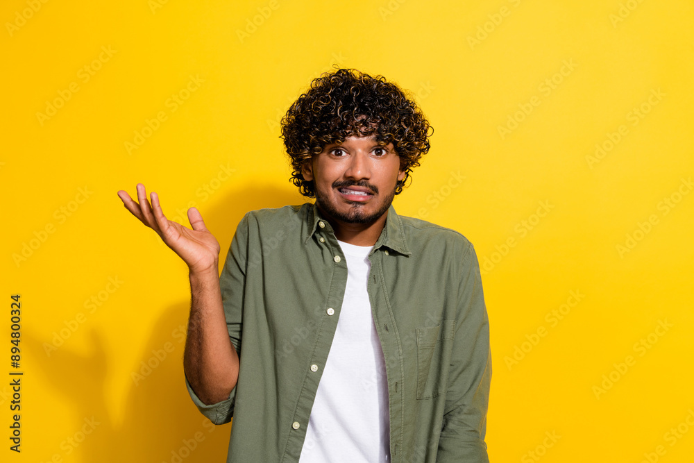 Portrait photo of young hispanic guy in khaki shirt confused raised hand questioned wtf no idea or isolated on yellow color background