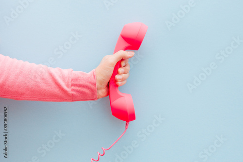 Communication and connection concept - woman hand with pink phone on light blue background