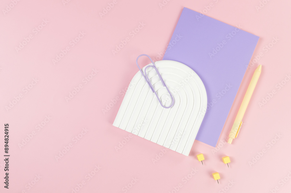 Top view of purple notebook, yellow pen, paperclip, pins, white arch tray on pink background. School, office wallpaper. Flat lay, copy space. Top view of purple notebook, yellow pen, paperclip, pins, white arch tray on pink background. School, office wallpaper. Flat lay, copy space.