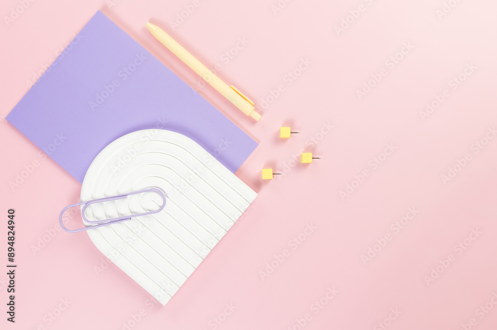 Top view of purple notebook, yellow pen, paperclip, pins, white arch tray on pink background. School, office wallpaper. Flat lay, copy space. Top view of purple notebook, yellow pen, paperclip, pins, white arch tray on pink background. School, office wallpaper. Flat lay, copy space.