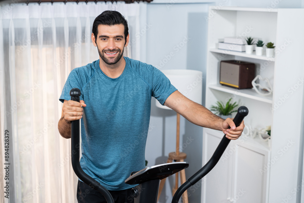 Athletic and sporty man running on elliptical running machine during home body workout exercise session for fit physique and healthy sport lifestyle at home. Gaiety home exercise workout training. Athletic and sporty man running on elliptical running machine during home body workout exercise session for fit physique and healthy sport lifestyle at home. Gaiety home exercise workout training.